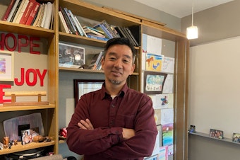 Pastor Peter Chin stands in his office. His office is decorated with kid drawings, family photos, and Mariners merch