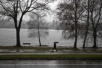 caption: A pedestrian walks along Green Lake on Friday, December 20, 2019, in Seattle.