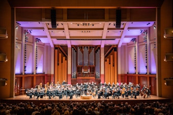 caption: The Seattle Symphony, led by Conductor Emeritus Ludovic Morlot, performing on stage in Benaroya Hall in 2023. 