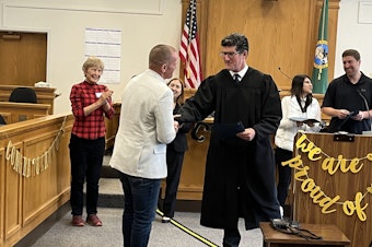 caption: King County Superior Court Judge John McHale congratulates drug court graduate Brandon Wright on Sept. 11, 2024. Judy Maleng, far left, is the widow of King County Prosecutor Norm Maleng, who founded the King County Drug Diversion Court in 1994.