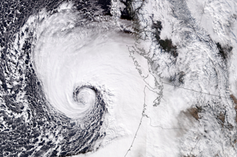 caption: This image taken by NASA shows a bomb cyclone over the Pacific Ocean, which sent heavy winds into Western Washington. The storm caused widespread power outages and property damage. Two people died from falling trees. 