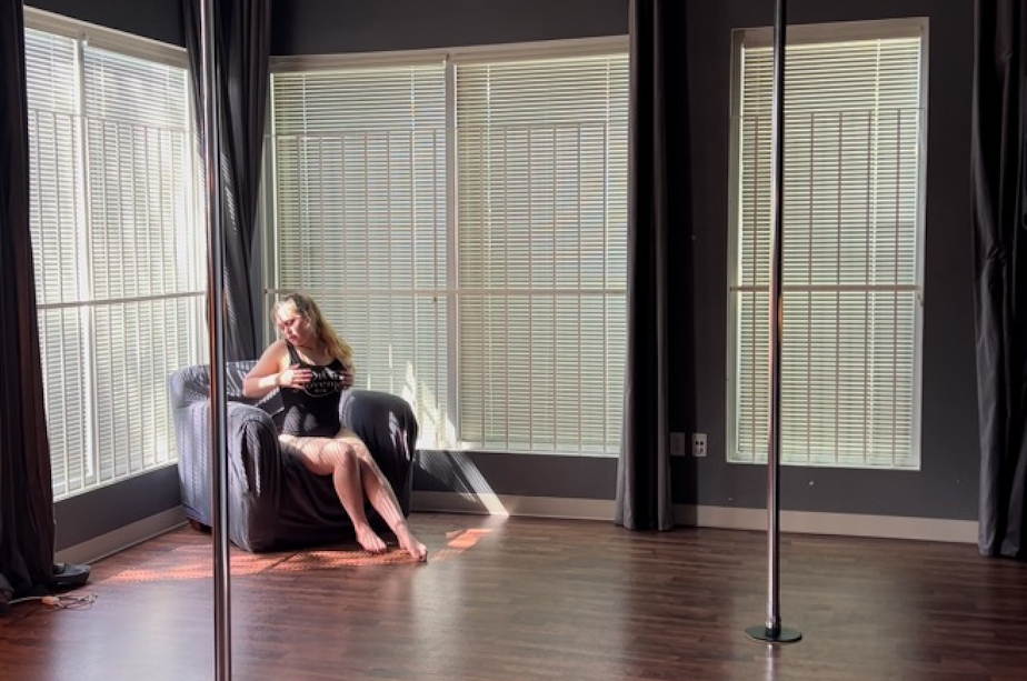 caption: Morgen White poses in her starting position before beginning a freestyle pole dance to the Nicki Minaj song "Grand Piano" at Divine Movement Pole Dance & Fitness in Seattle in May 2022. 